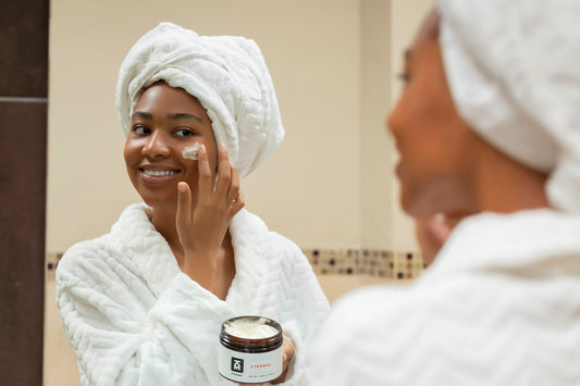 Mujer con toalla en la cabeza aplicándose crema en la cara frente al espejo